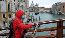 A man wearing a protective mask paint on Accademia bridge in Venice on March 8, 2020 on March 8, 2020 in Venice shows the Grand Canal empty of boats with the Salute Church on the left. - A quarter of the Italian population was locked down on March 8, 2020 as the government takes drastic steps to stop the spread of the deadly new coronavirus that is sweeping the globe, with Latin America recording its first fatality. (Photo by ANDREA PATTARO / AFP) (Photo by ANDREA PATTARO/AFP via Getty Images)